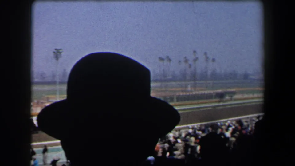 1958 California racetrack footage framed by a spectator's hat silhouette, with horses and a crowd visible beyond the rail.