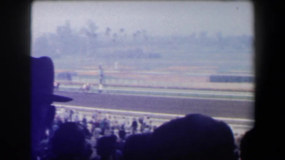 1958 California racetrack view with horses and jockeys passing below silhouetted spectators in the stands.