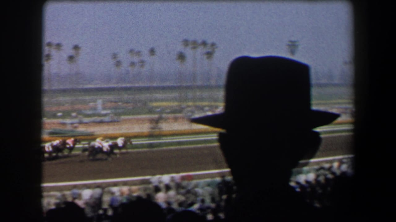 1958 California home-movie view from grandstands, with fedora silhouettes in front of horses racing past palm trees.