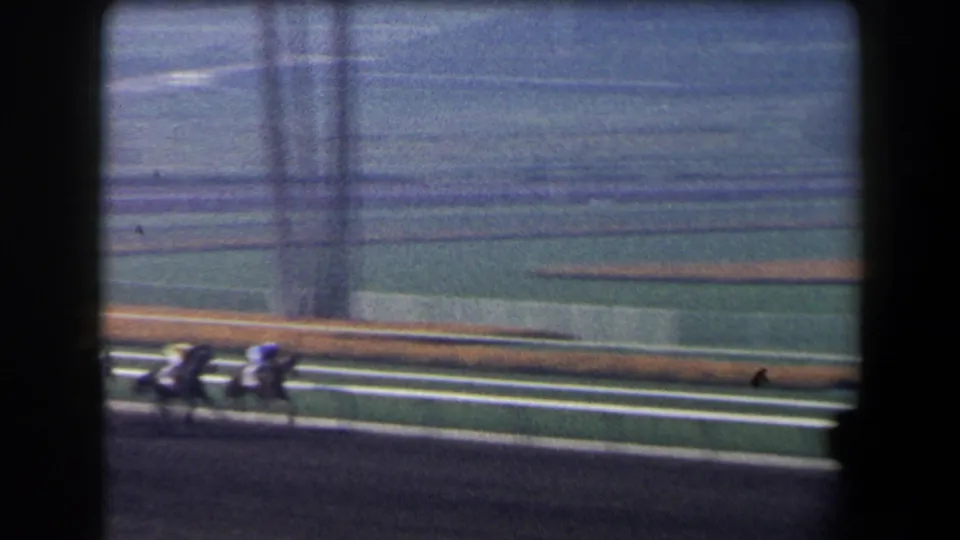 1958 California racetrack view showing a small group of horses and jockeys moving along the rail in soft 8mm color.