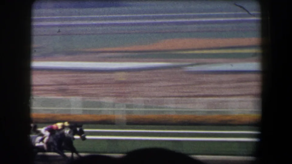 A horse and jockey move quickly along the California racetrack, with white rails, turf, and blurred infield lanes behind them.
