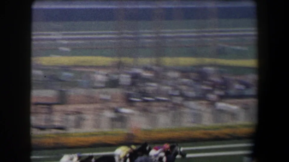 In this 1958 California 8mm frame, horses and jockeys blur across the lower track as spectators fill the grandstand behind them.
