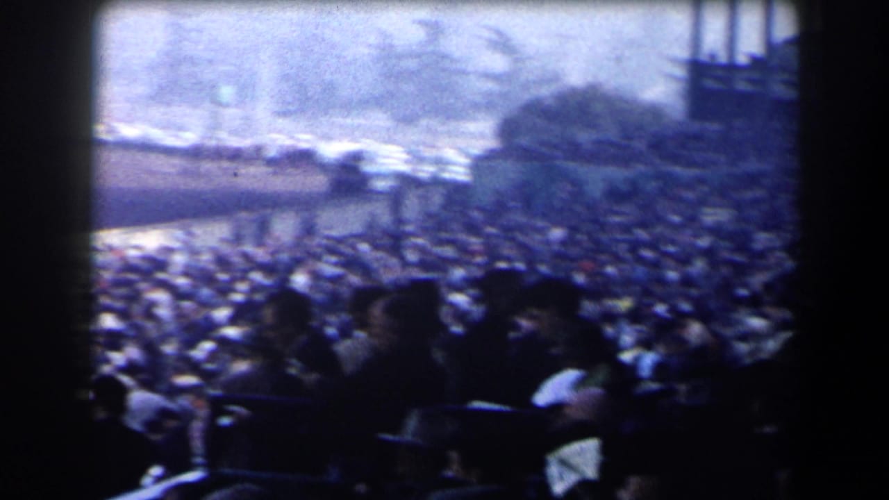 1958 California home-movie view of packed racetrack stands with spectators watching from a shaded position.