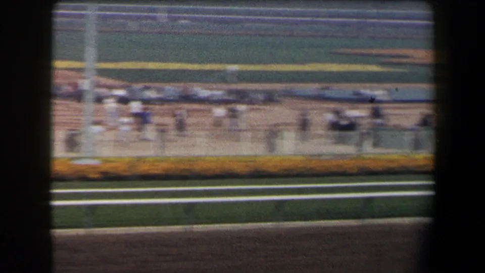 1958 California horse track scene with scattered spectators near the rail, infield plantings, and distant grandstand areas during a slow pan.