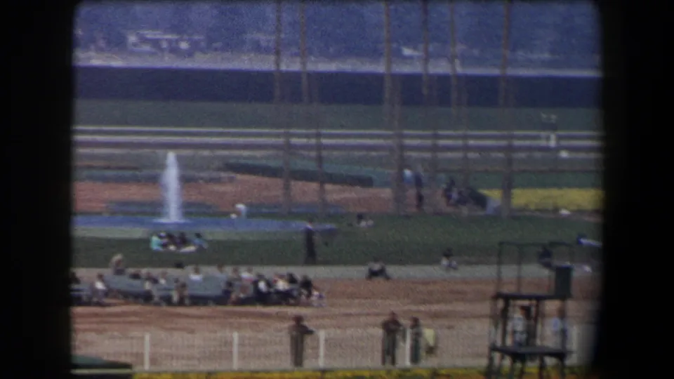 1958 California 8mm view of the racetrack infield with seated spectators, railings, a small trackside structure, and distant posts.