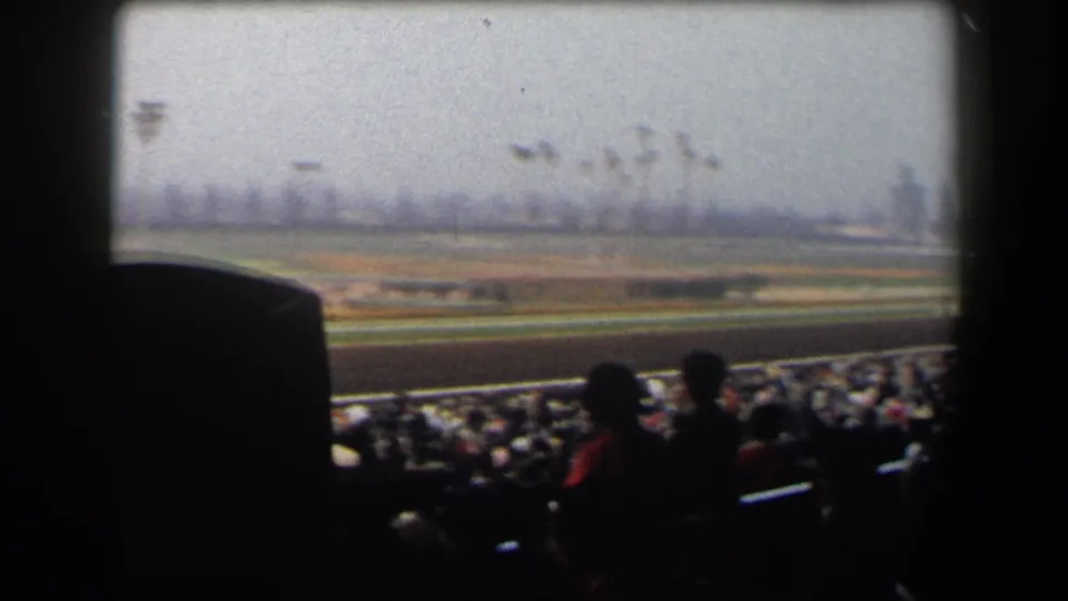 Spectators in a California racetrack grandstand watch horses run along the rail in faded 8mm footage from 1958.