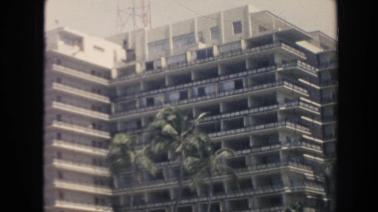 High-rise hotel balconies behind palm trees near a sandy beach.