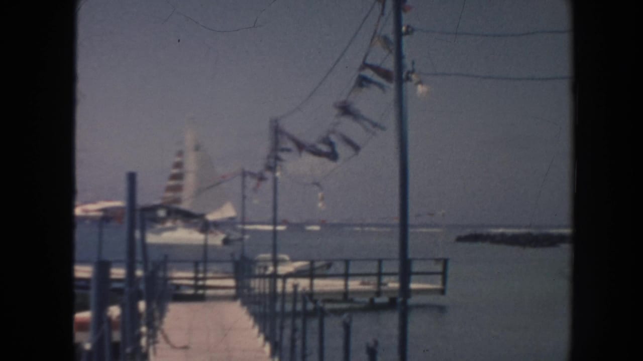 Waterfront pier with pennant flags and a striped sailboat beyond it.