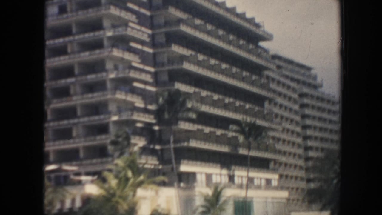 Large multi-story balcony building with palm trees in front.