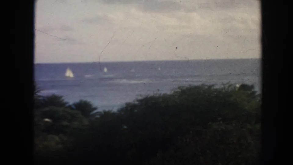 1961 Hawaii coastal view with sailboats on the ocean, cloudy sky, and dark vegetation along the lower frame.