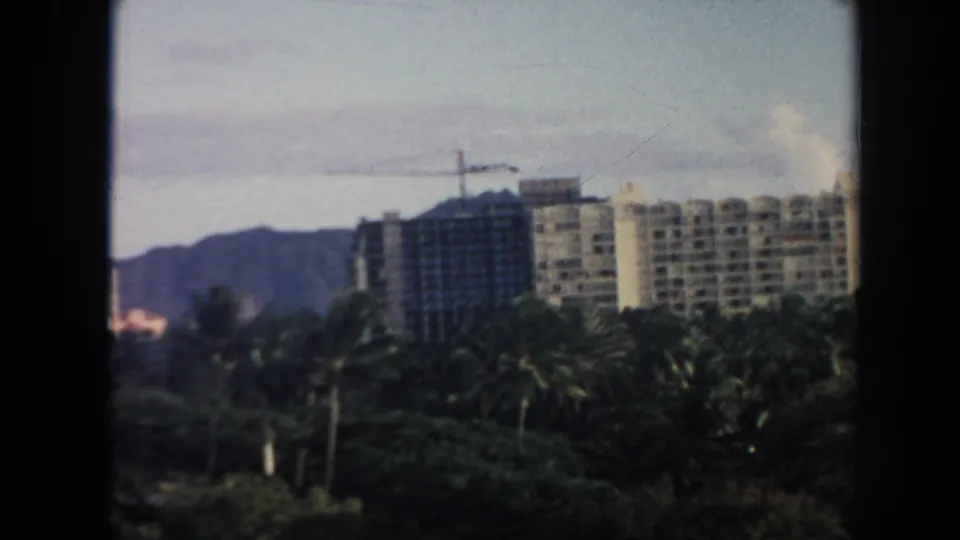 1961 Hawaii home-movie view of high-rise buildings under construction, palms, and distant mountains through a window frame.