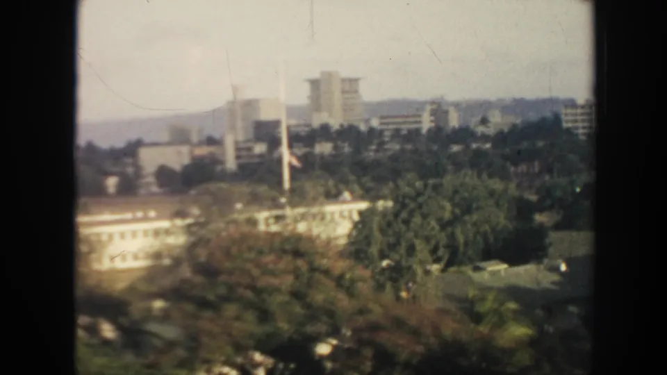 1961 Hawaii elevated view with white buildings, trees, flagpoles, and distant high-rises under hazy daylight.