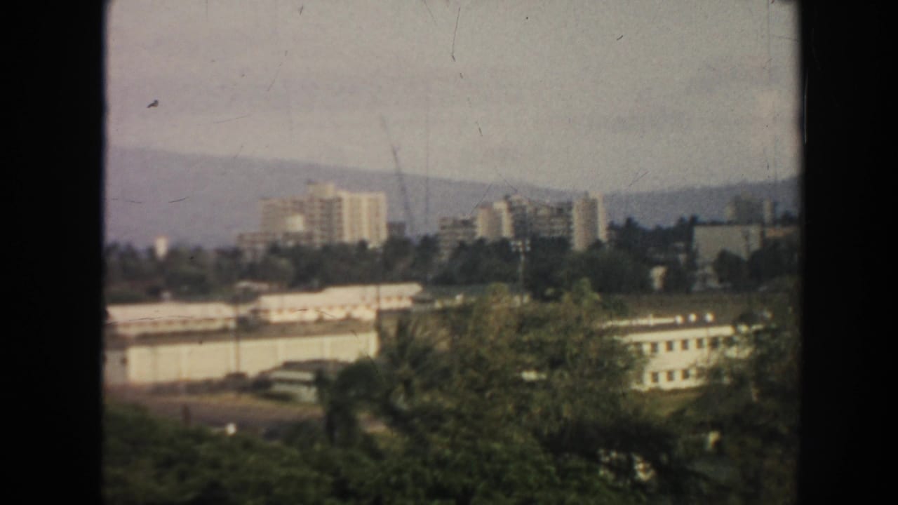 1961 Hawaii 8mm frame showing a coastal city panorama with high-rises, greenery and distant mountains.