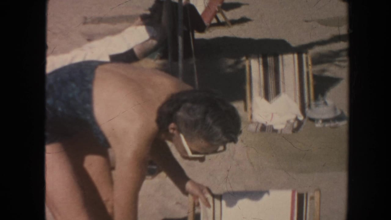 1961 Hawaii beach frame with an adult woman in cat-eye sunglasses leaning over a striped folding chair.
