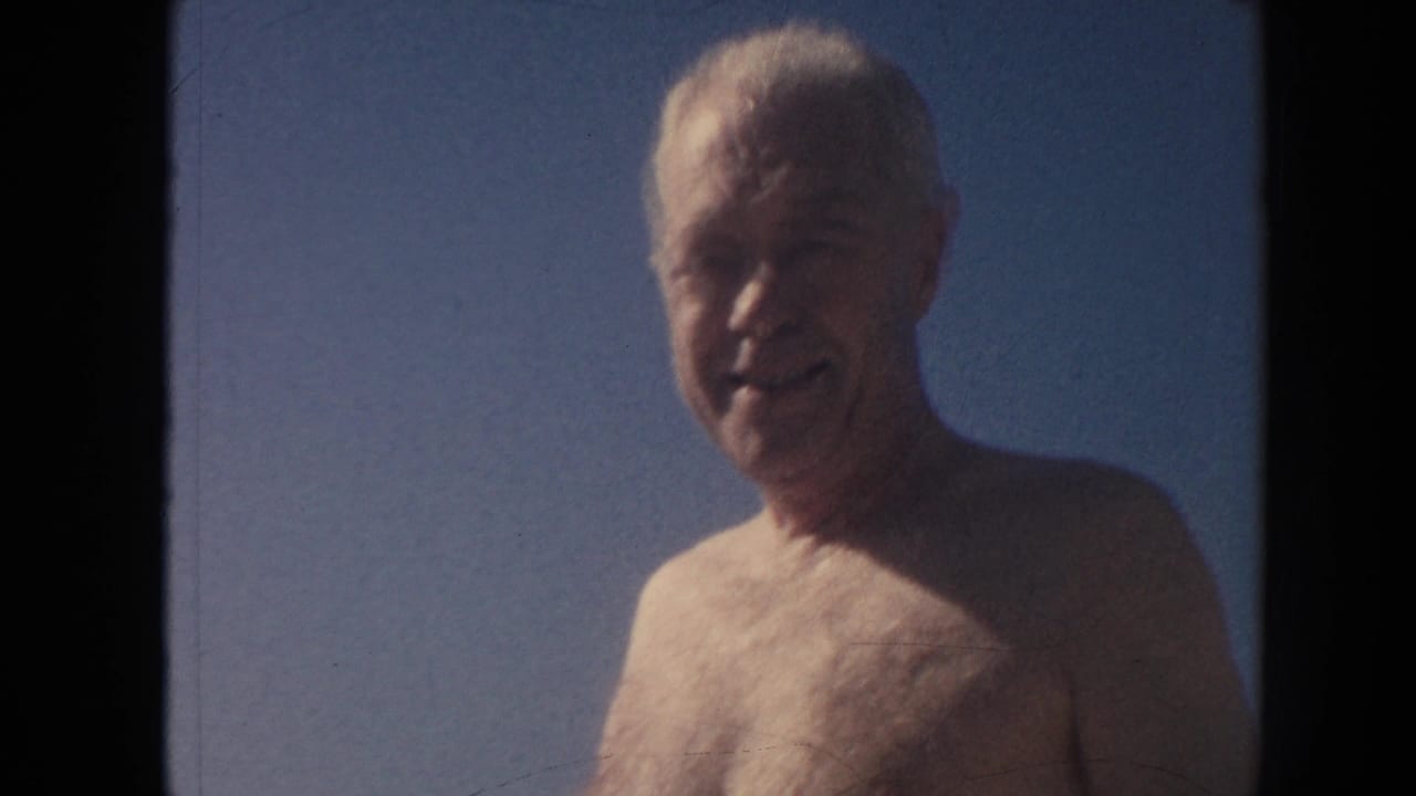Shirtless older man smiling with blue sky behind him.
