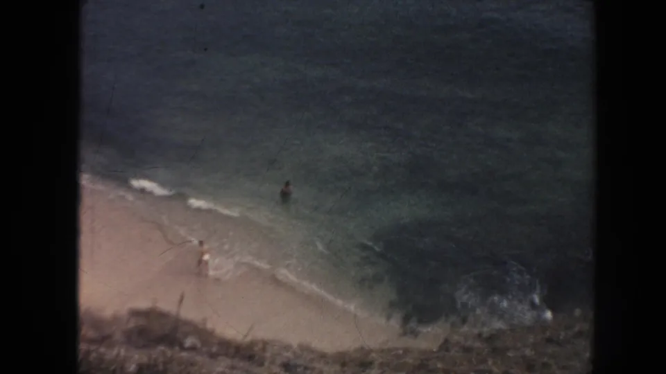 1961 Hawaii beach view with pale sand, turquoise shallows, small swimmers, and surf along the shoreline.