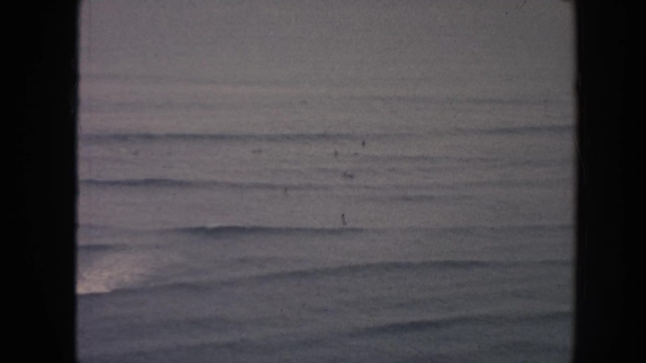 Soft ocean swells under an overcast sky, framed by dark film gate edges.