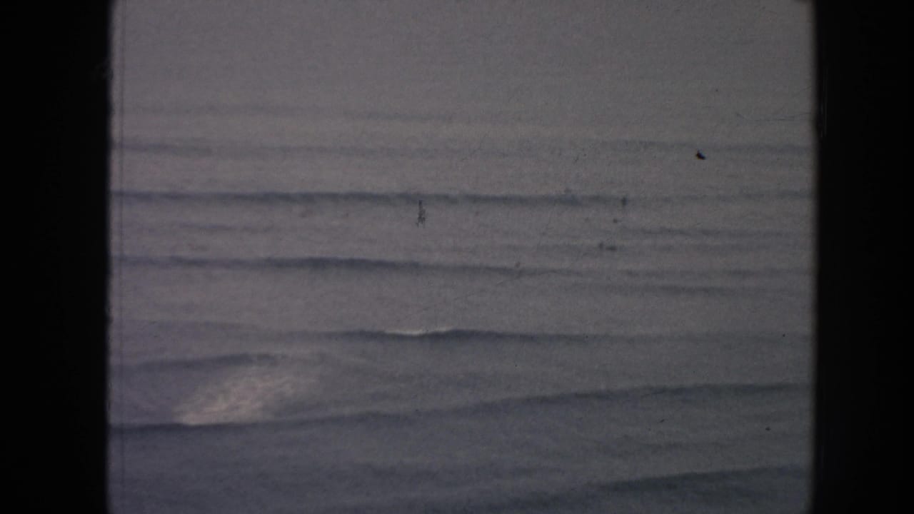 1961 Hawaii coastal water view with low rolling waves, muted light, and dark vertical film gate borders.