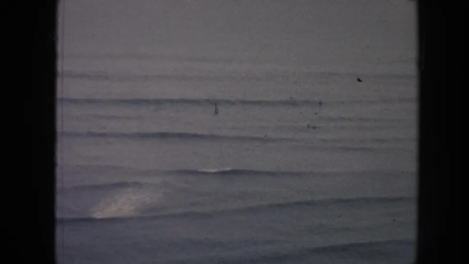 1961 Hawaii coastal water view with low rolling waves, muted light, and dark vertical film gate borders.