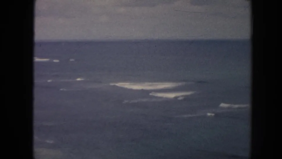 1961 Hawaii 8mm frame widening to offshore water, white surf breaks, and a dark overcast horizon.