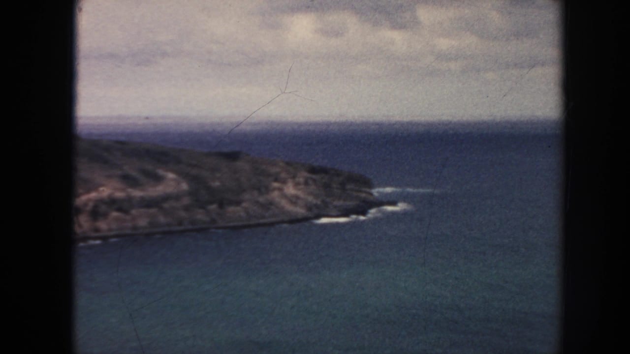 1961 Hawaii 8mm frame looking down toward a rugged coastline, open ocean, and cloudy sky from an elevated vantage point.