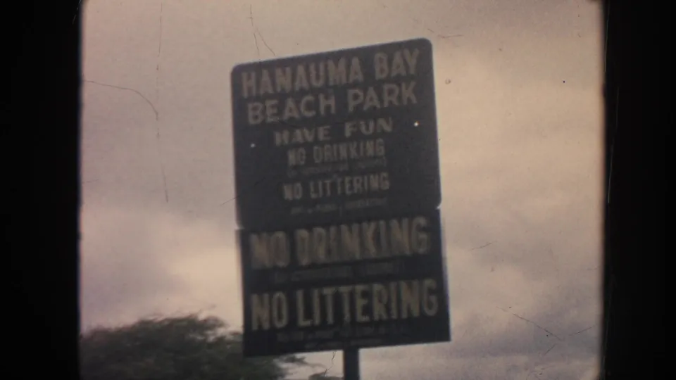 1961 Hawaii frame showing a Hanauma Bay Beach Park rules sign, including visible no drinking and no littering notices.
