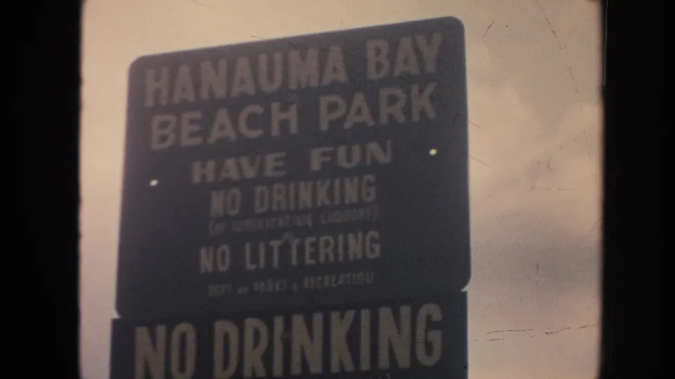 1961 Hawaii 8mm frame showing a Hanauma Bay Beach Park rules sign under cloudy sky.