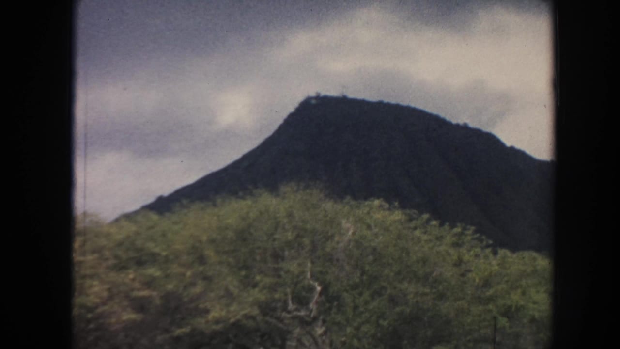 1961 Hawaii 8mm frame with a rounded dark peak above dense vegetation and a muted cloudy sky.