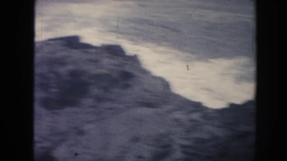1961 Hawaii 8mm frame of a rugged rock edge with pale turbulent water behind it and visible film-gate borders.