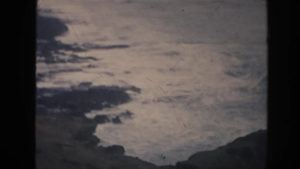 1961 Hawaii 8mm frame with pale, restless ocean water between dark rock shapes and visible film wear.