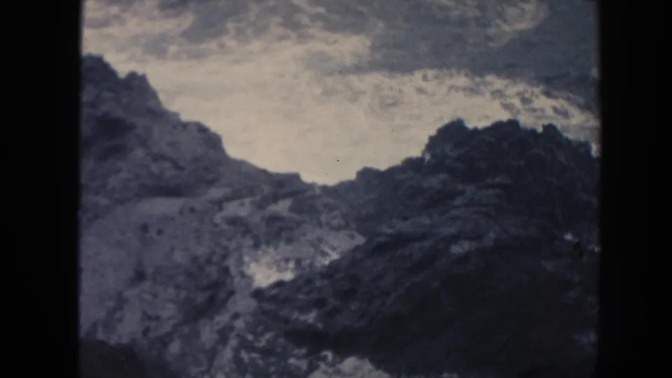 1961 Hawaii 8mm frame showing foamy water spreading over dark volcanic-looking rocks along a rugged coast.