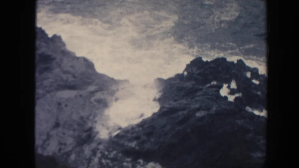 1961 Hawaii 8mm frame showing breaking white surf in a rocky coastal channel, with dark rocks framing the water.