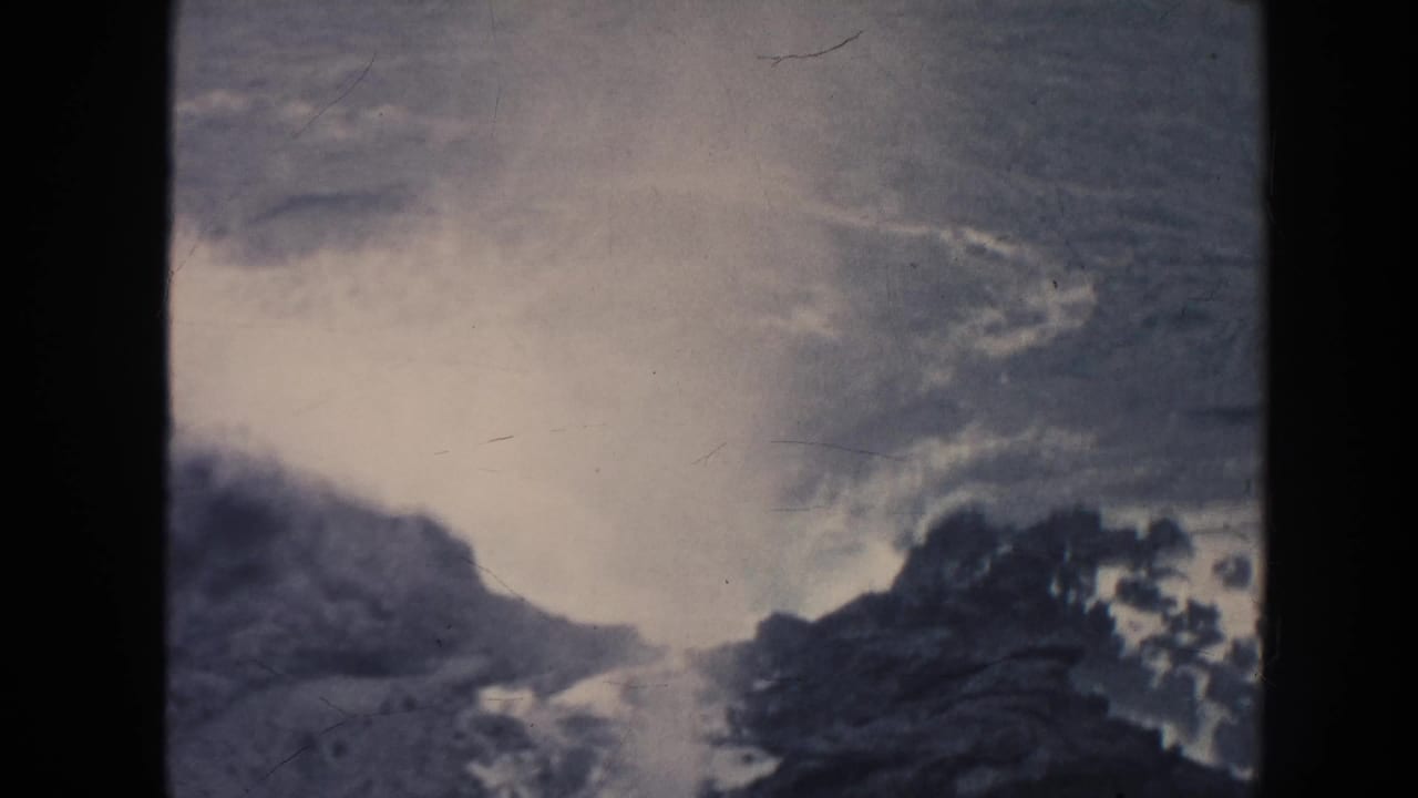1961 Hawaii 8mm frame showing pale surf breaking over a rocky shoreline under a muted, cloudy sky, with heavy film borders visible.