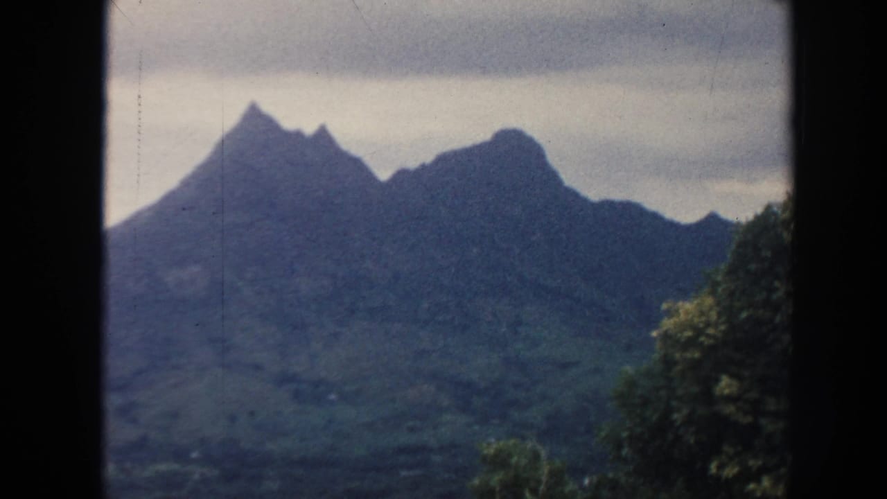 Dark-framed view of jagged green mountain peaks beneath a pale sky.