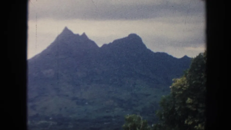 1961 Hawaii 8mm frame showing jagged mountain peaks, green slopes, soft sky, and dark film borders.