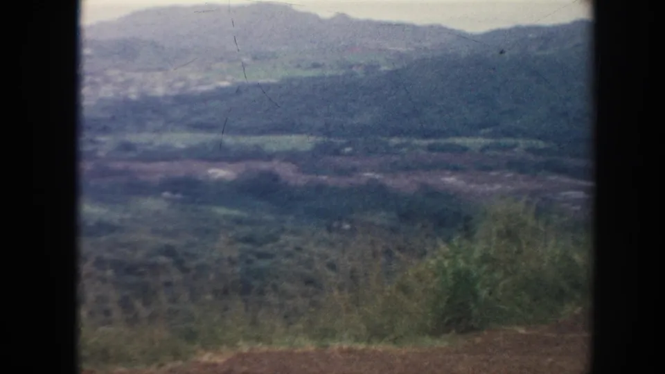 1961 Hawaii 8mm frame showing a wide verdant valley, foreground shrubs, hazy mountain ridges, and visible film wear.