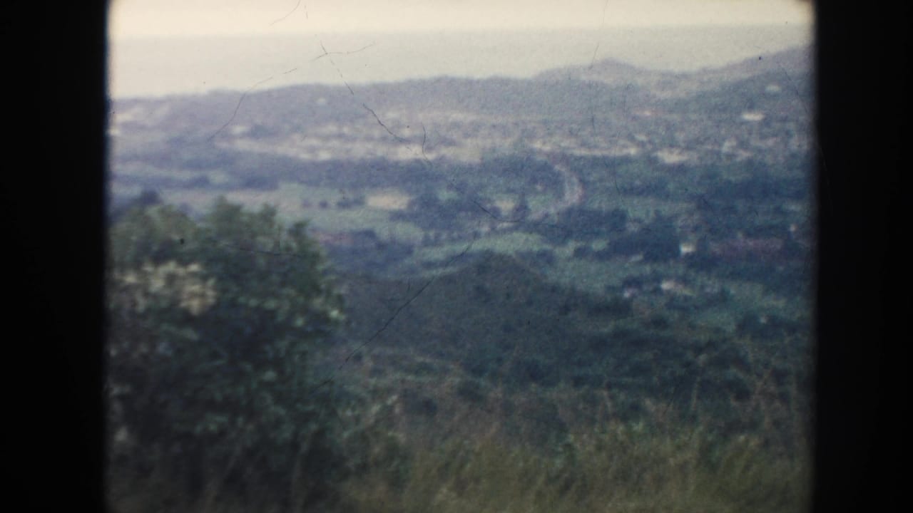 Distant green valley and hills seen from a high overlook through dark film borders.