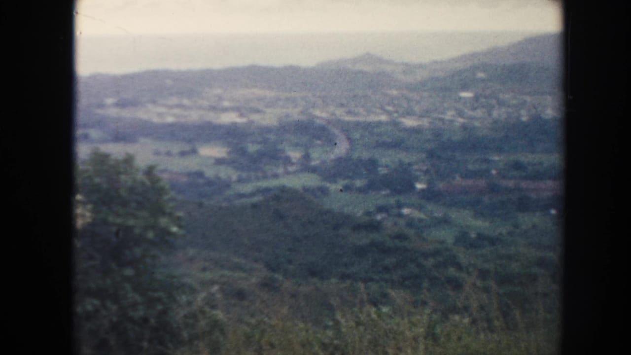 Rolling countryside with fields, distant hills, and a winding road under cloudy sky.