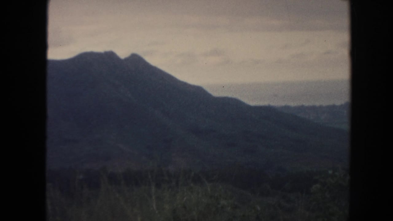 1961 Hawaii 8mm frame showing distant green mountain ridges and a cloudy sky through dark projector-like borders.