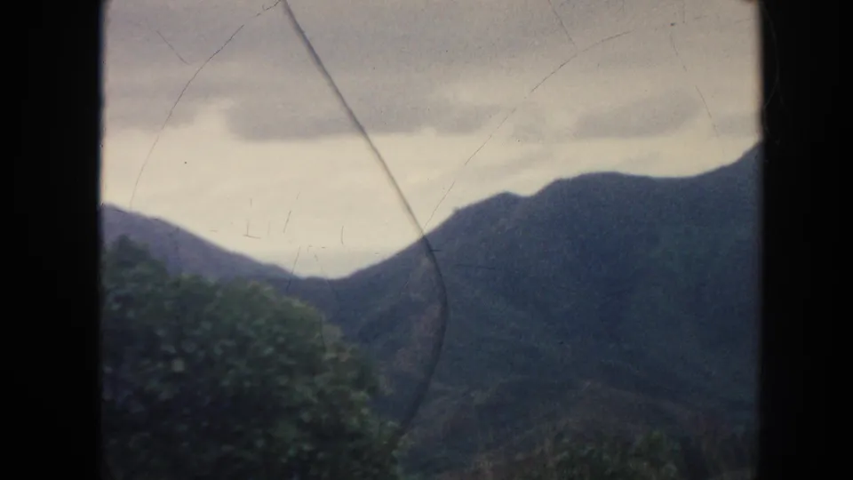 1961 Hawaii 8mm frame with foreground vegetation, dark mountain slopes, and visible film scratches.