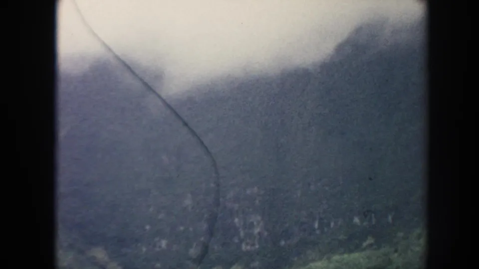 1961 Hawaii home-movie frame showing a hazy green mountainside and valley with pronounced 8mm surface marks.