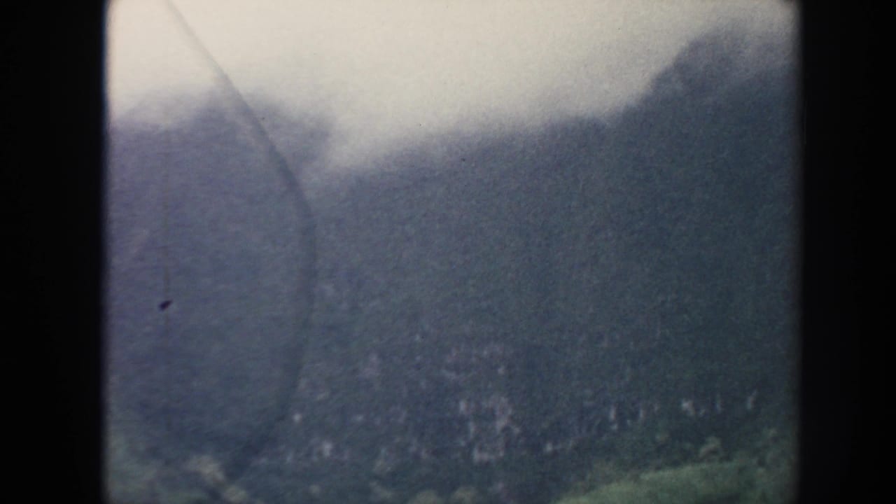 1961 Hawaii 8mm frame showing a dark mountain ridge partly covered by cloud, with green forest below and visible film scratches.