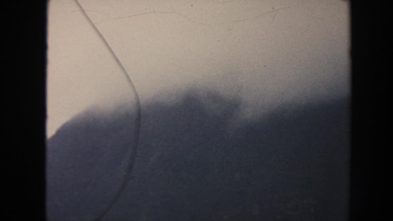 1961 Hawaii 8mm frame with a cloud-softened mountain ridge under an overcast sky and prominent vertical film gate edge.