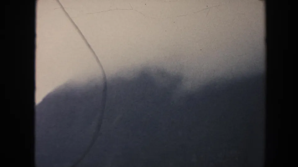 1961 Hawaii 8mm frame with a cloud-softened mountain ridge under an overcast sky and prominent vertical film gate edge.