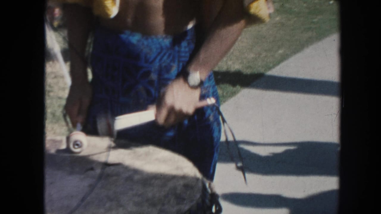 A close 1961 Hawaii frame shows the performer's torso, blue patterned shorts, drumsticks, and the top of a large outdoor drum.