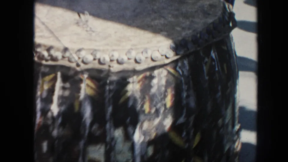 The frame focuses on a large hide-covered drum with a laced rim and patterned fabric, seen from a close visitor-shot angle.