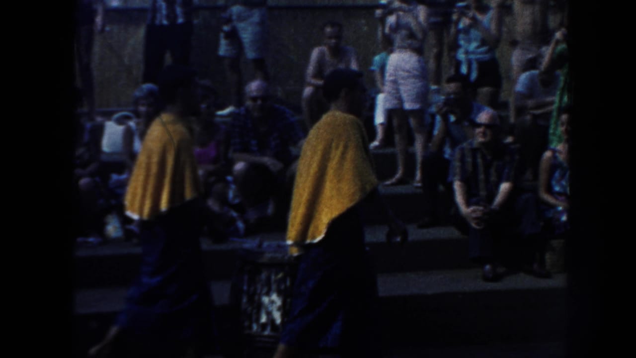Two performers in yellow capes stand before seated spectators at an outdoor gathering.