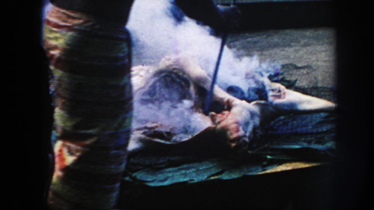 A 1961 Hawaii home-movie frame shows a person using a long tool near smoking meat or a carcass on leaves.