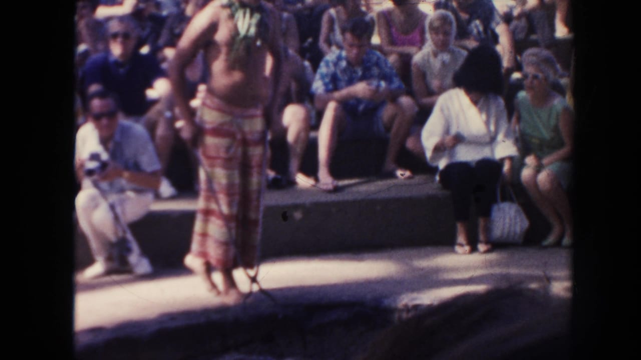 Performer in red and yellow wrap stands before seated spectators.
