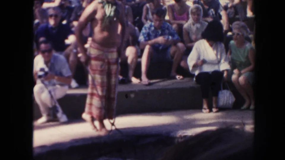 A barefoot performer in a red and yellow wrap stands before a seated outdoor audience in Hawaii, 1961.